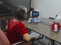 A woman sits with 2 social robots